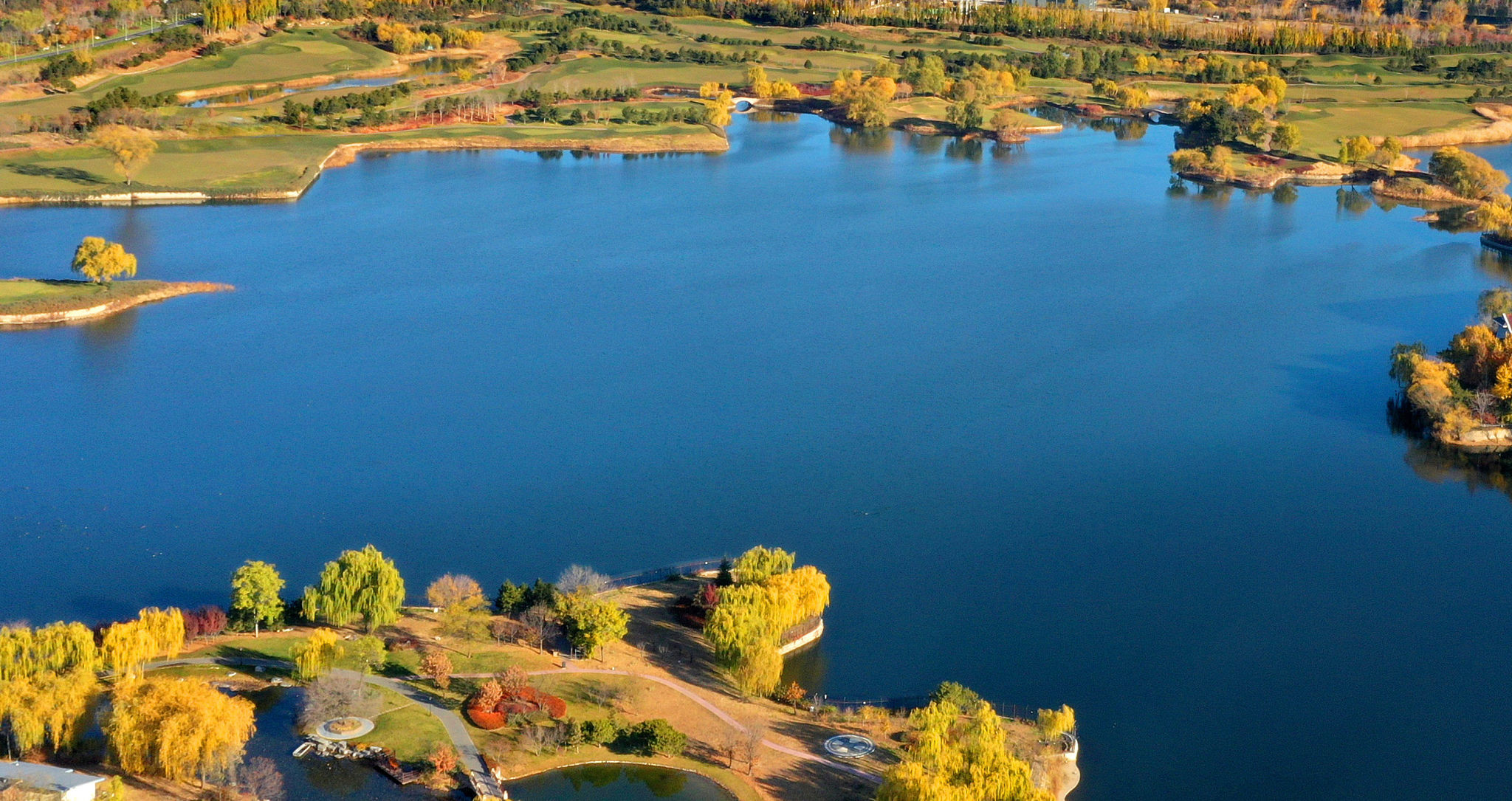 航拍镜头下的北京怀柔雁栖湖晚秋景色,湖水湛蓝,草树茂密.