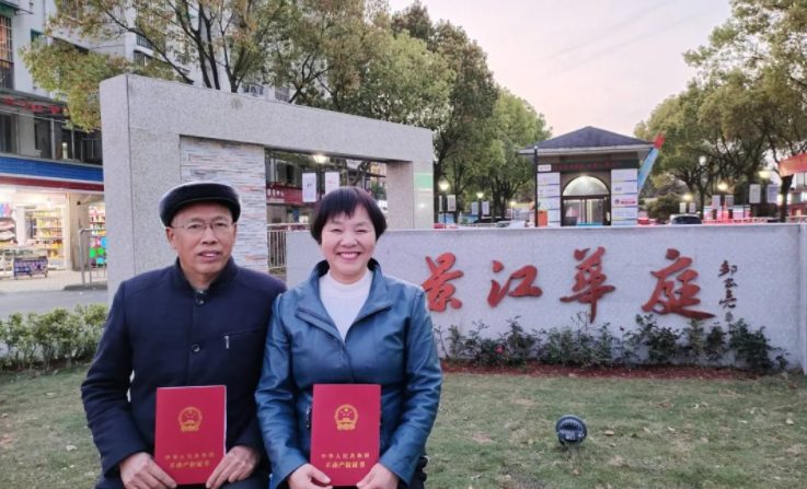 近日，居民王师傅两口子拿着更名后的新房产证在新小区门口合影留念。