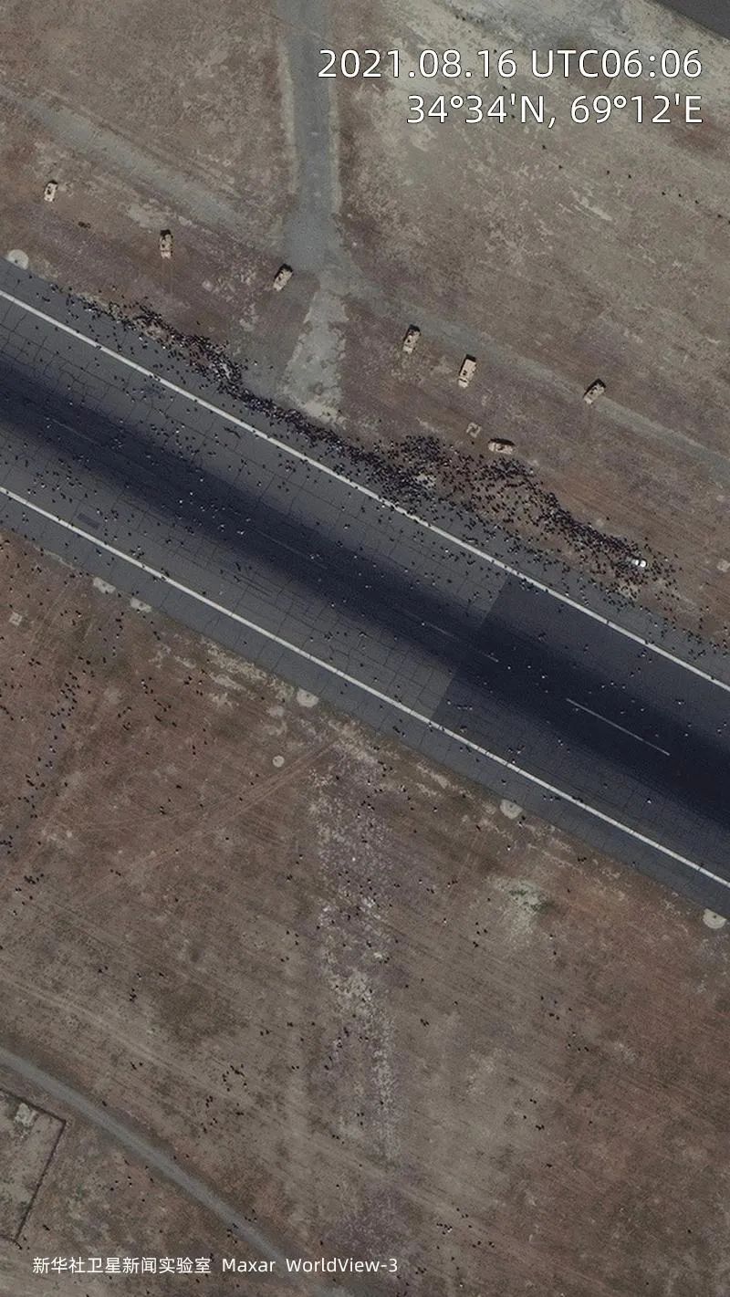 喀布尔国际机场，等待撤离的人群涌入停机坪，横穿起飞区域，在机场唯一的跑道旁聚集。数辆美军车辆在人群附近监视。