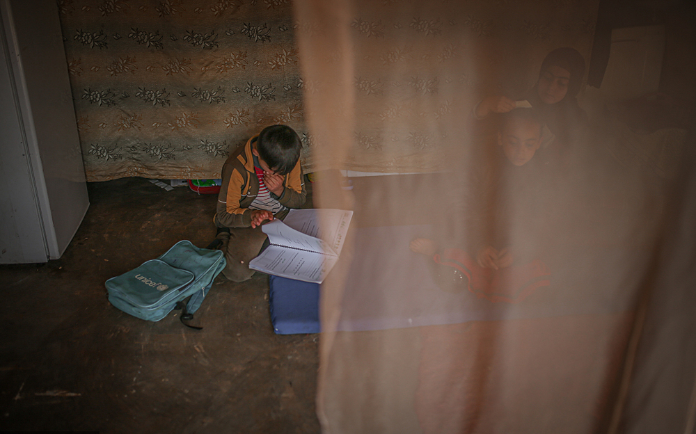 当地时间2022年3月8日,叙利亚伊德利卜,在当地一座难民营里,一个小朋友在昏暗的室内读书。人民视觉 资料图