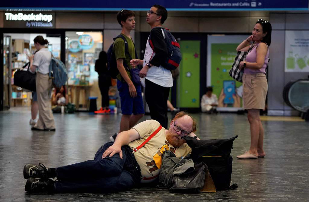 当地时间2022年7月19日,英国伦敦,市中心尤斯顿火车站乘客们带着随身物品坐在地上。由于铁轨边的火灾和英国经历的极端热浪,铁路服务被取消。