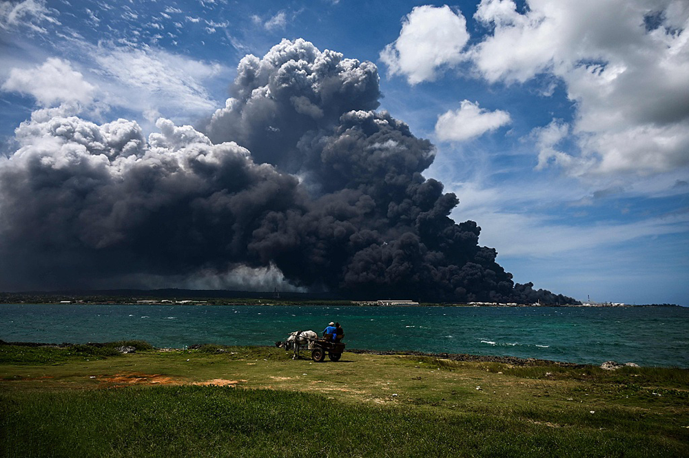 当地时间2022年8月8日，古巴马坦萨斯，人们坐在马车上看着燃料仓库火灾产生的黑烟。